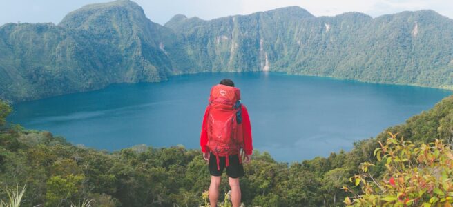 Hiker with backpack enjoying scenic mountain lake view on a bright summer day.